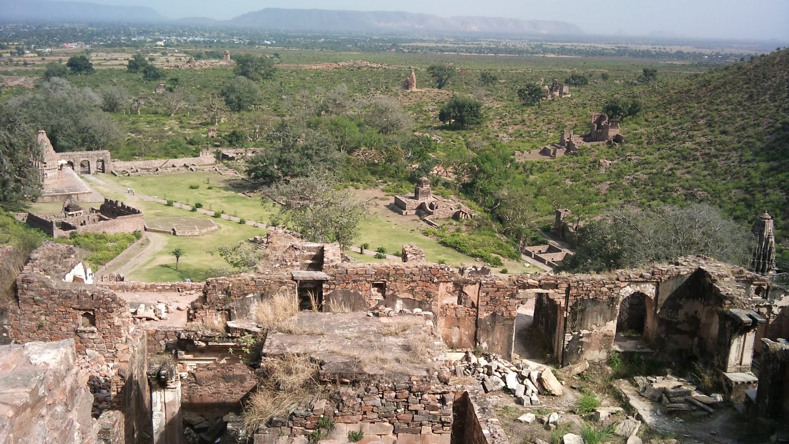 Roofless stone ruins of the old town of Bhangarh among trees, with the Aravalli hills behind