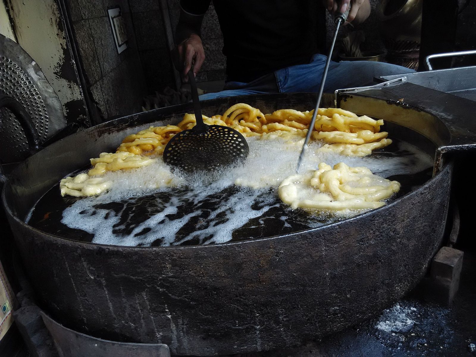 Spirals of golden jalebi frying in a wide iron pan at a sweet shop in Old Delhi