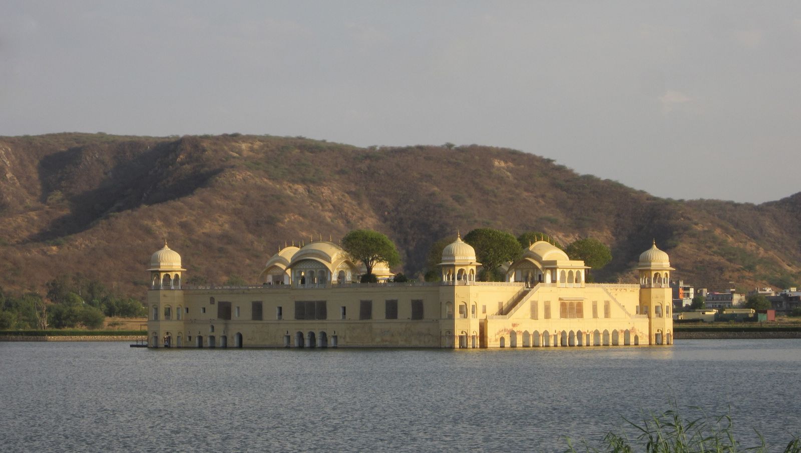 Jal Mahal, a sandstone palace with corner domes, rising from the still water of Man Sagar Lake in Jaipur with the Aravalli hills behind