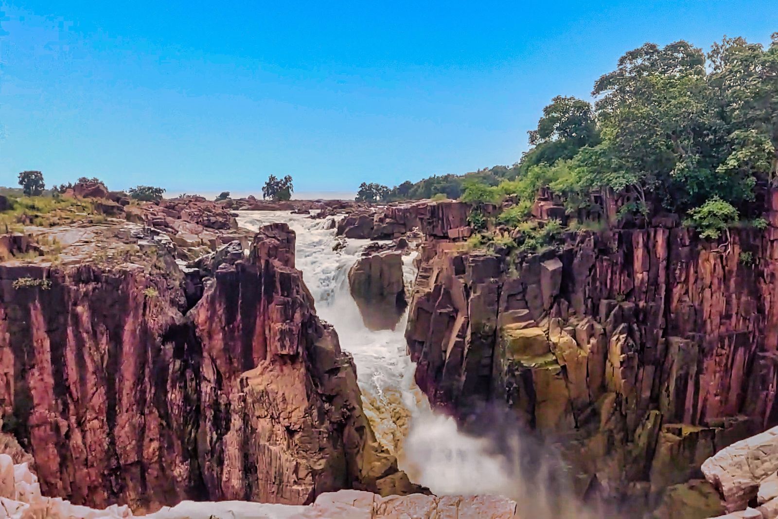 Water falling over bands of pink and grey crystalline granite in the Ken River canyon at Raneh Falls