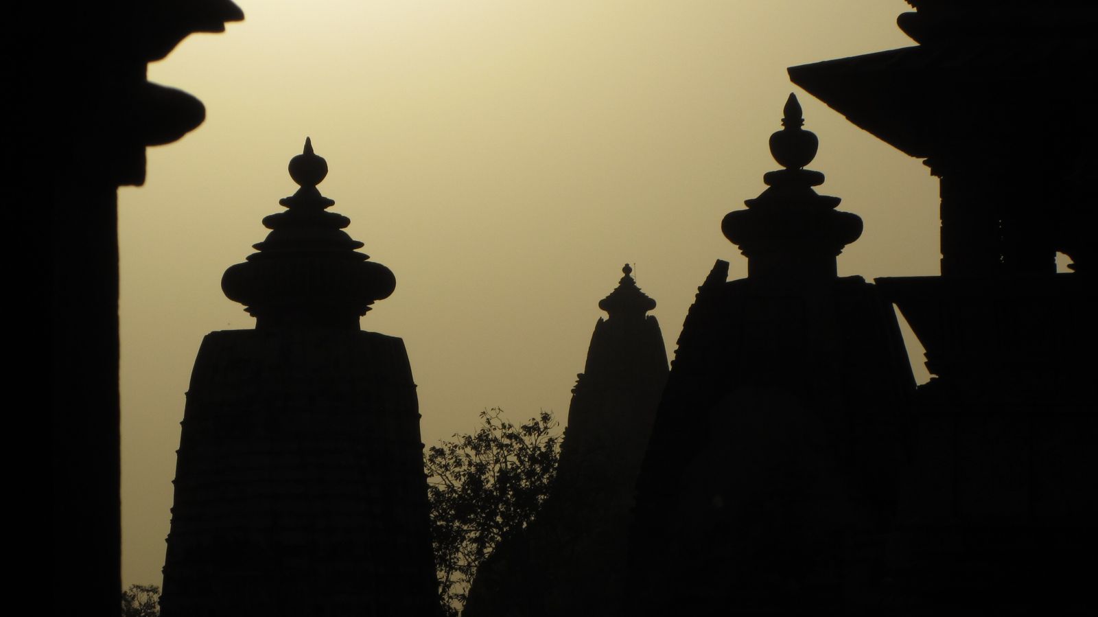 The spires of the Khajuraho temples silhouetted against a pink and orange evening sky