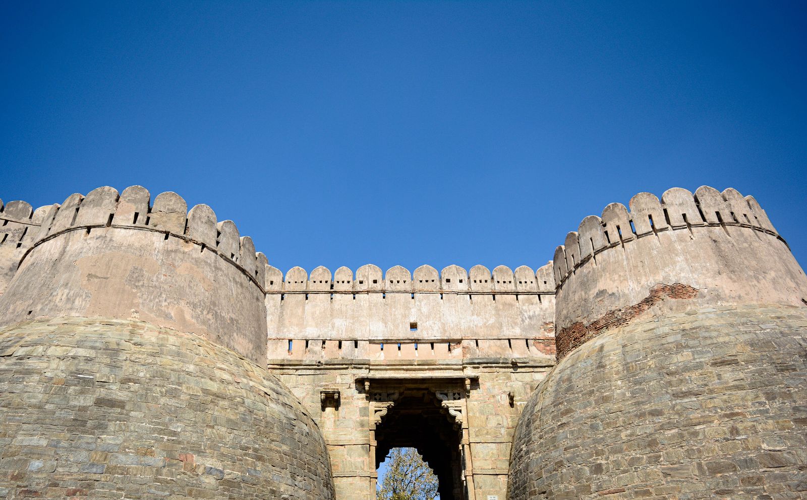A massive stone gateway with round bastions leading up into Kumbhalgarh Fort