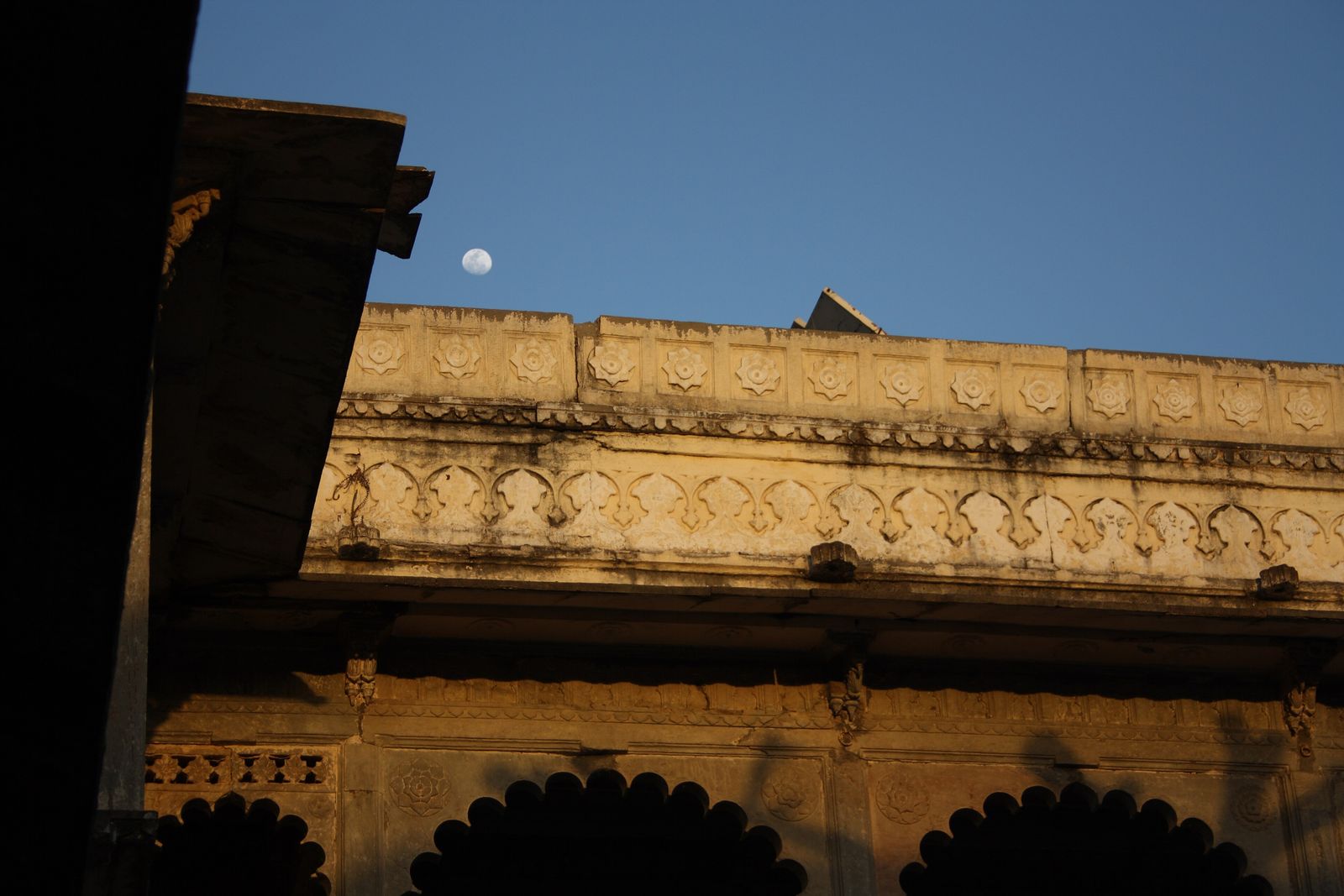 The courtyard of Bagore ki Haveli in Udaipur at dusk, with the moon rising above its arches