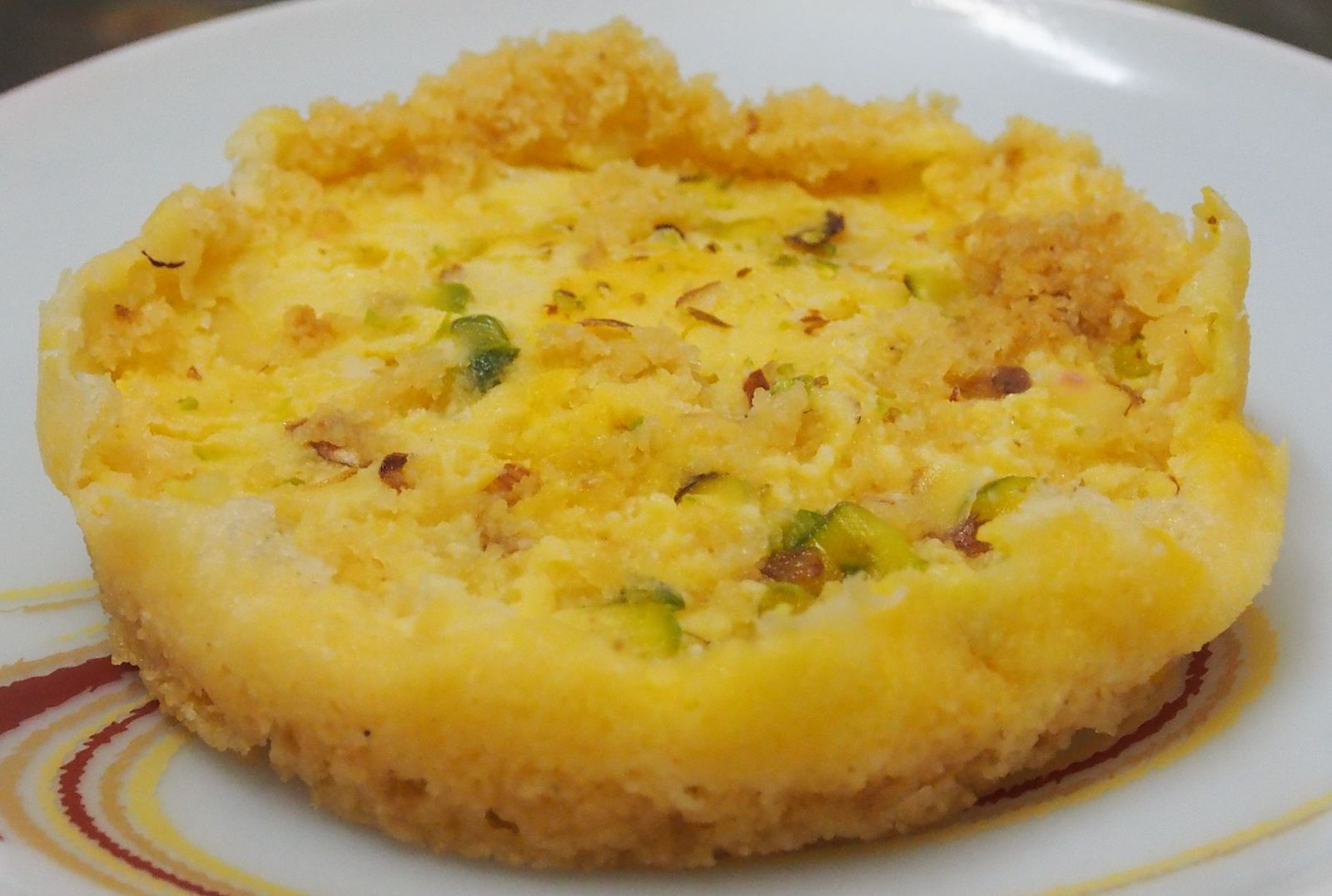 A round ghevar, the honeycomb sweet of Rajasthan, topped with a layer of malai cream