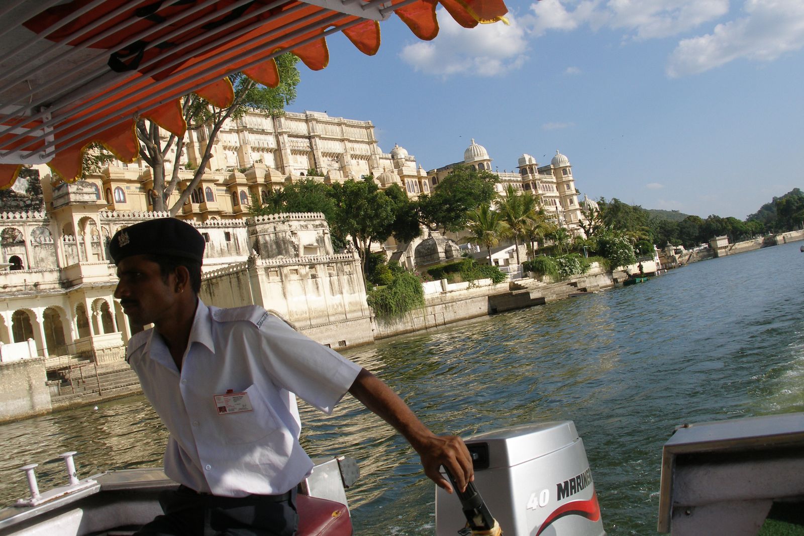 A small boat crossing Lake Pichola in Udaipur at sunset with the City Palace on the shore behind
